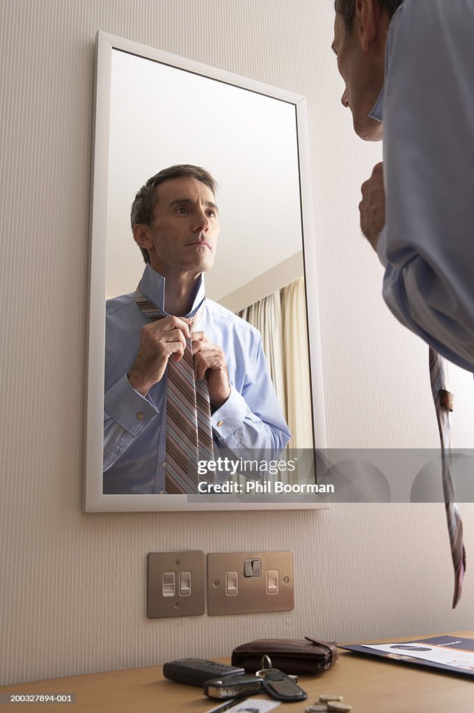 Businessman putting on tie in mirror of hotel bedroom