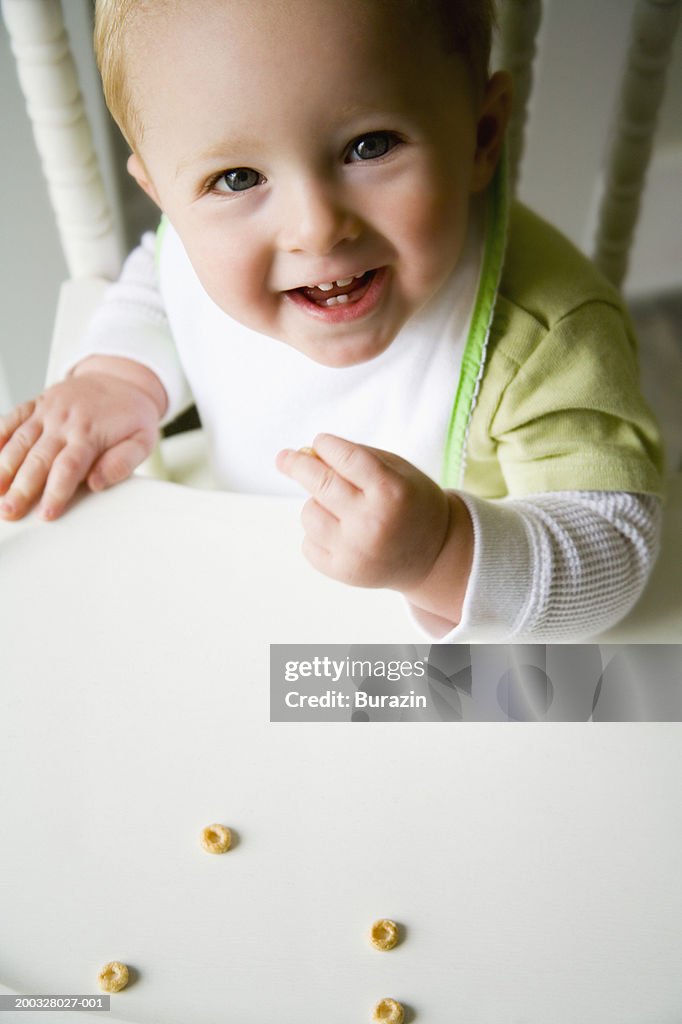 Baby boy (12-15 months) in high chair eating cereal, portrait