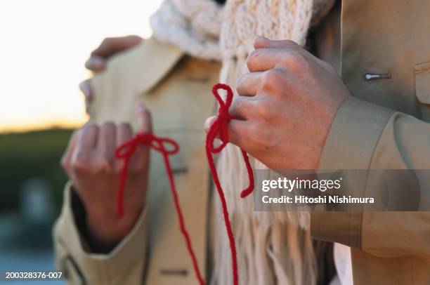couple with tied knots in finger outdoors, mid section - rode draad stockfoto's en -beelden