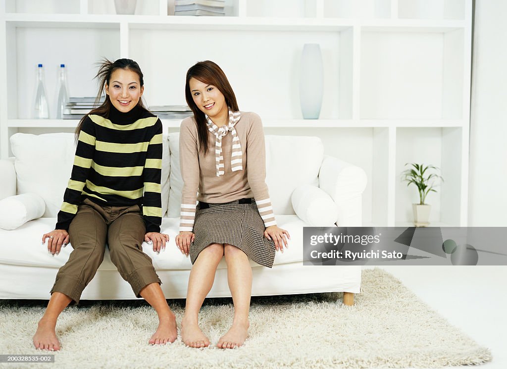 Two young women sitting on sofa, smiling, portrait