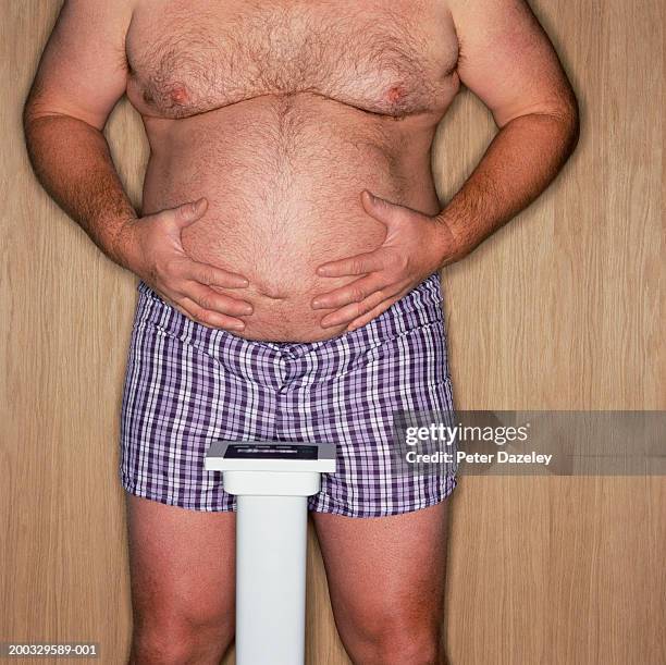 mature man standing on scales holding belly, mid section - pens stockfoto's en -beelden