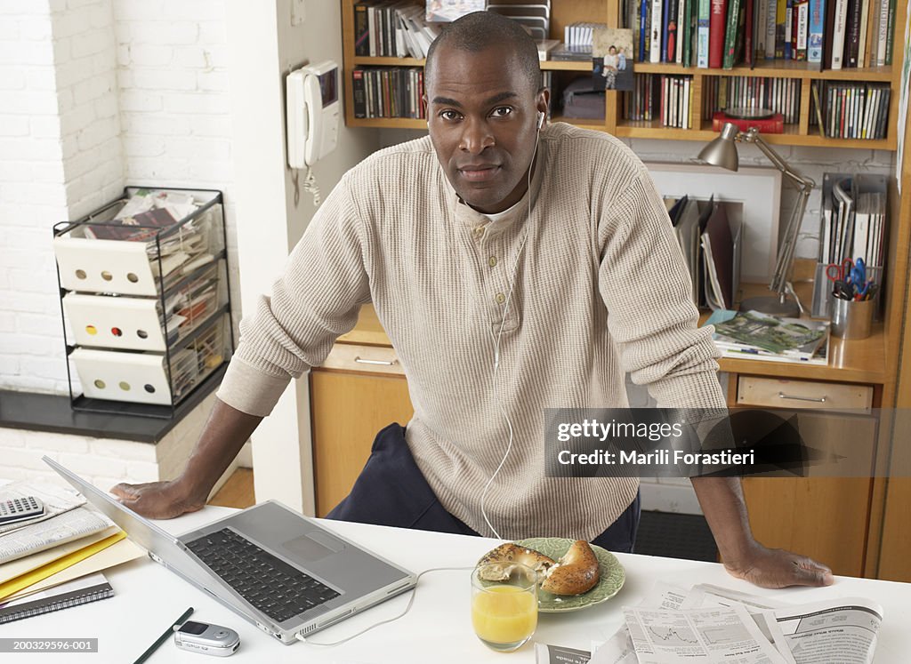 Mature man in home office, wearing earphones by laptop, portrait