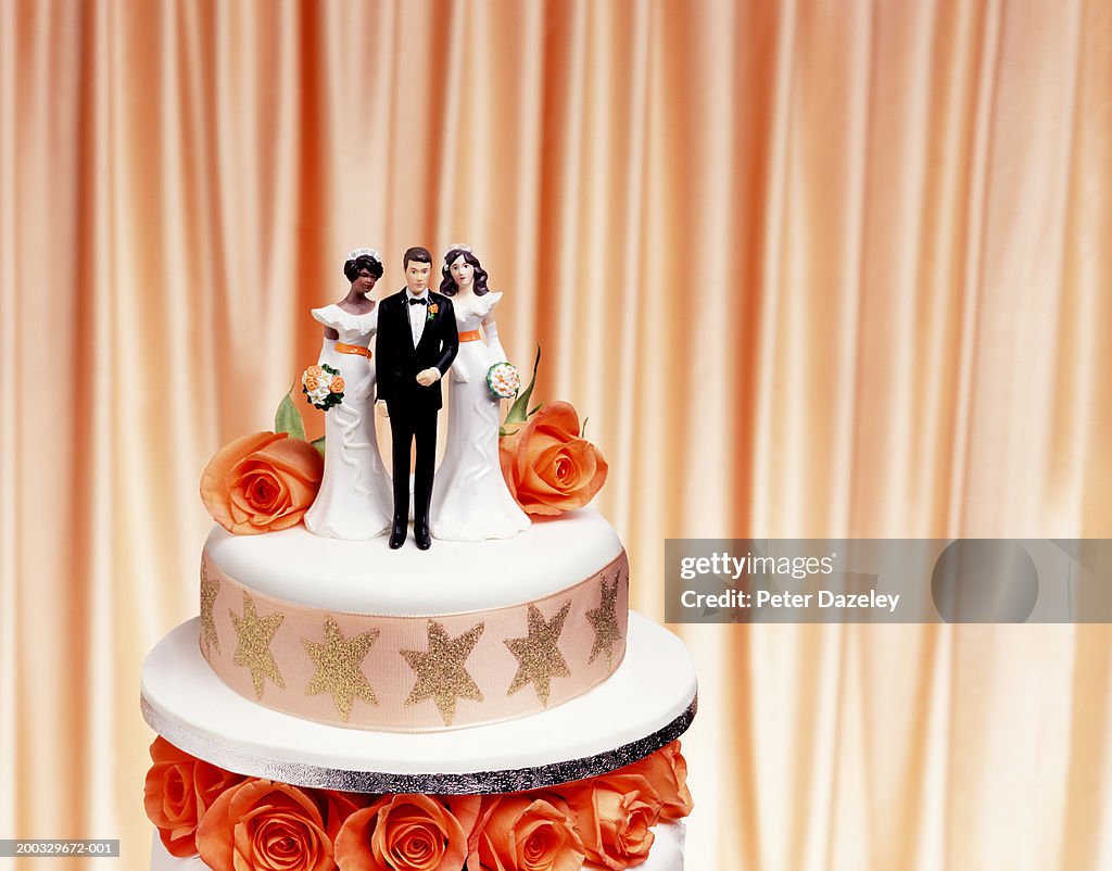 Groom and two bride figurines on top of wedding cake, close up