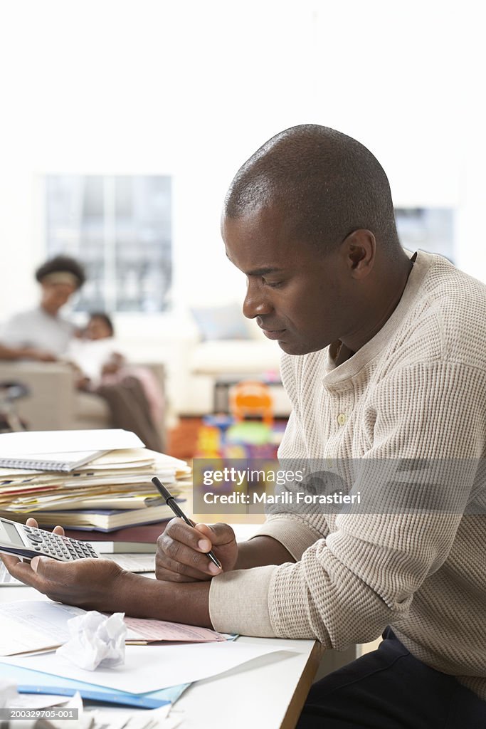 Man using calculator, mother with baby girl (6-9 months) in background