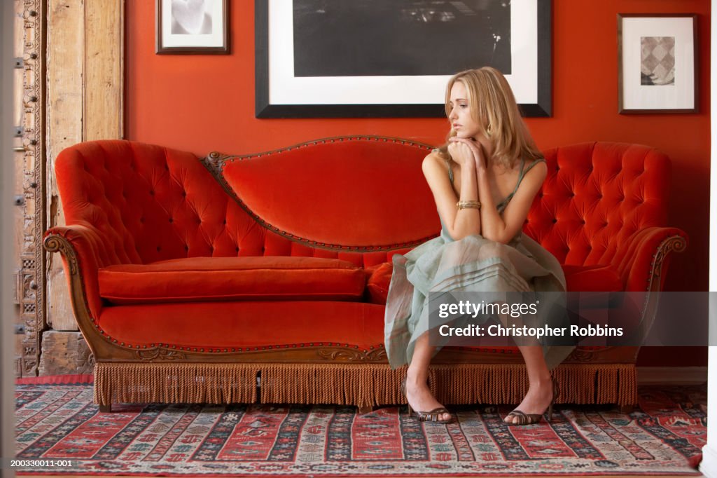 Young woman sitting on sofa, resting elbows on knees, looking to side