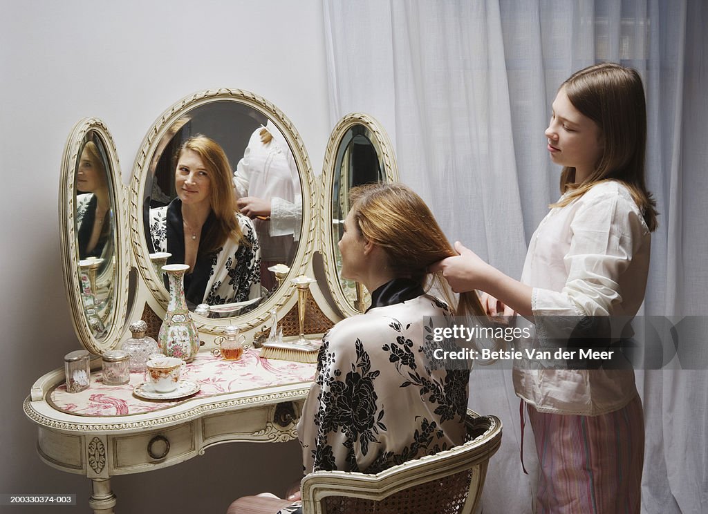 Girl (10-12) brushing mother's hair by bedside mirror