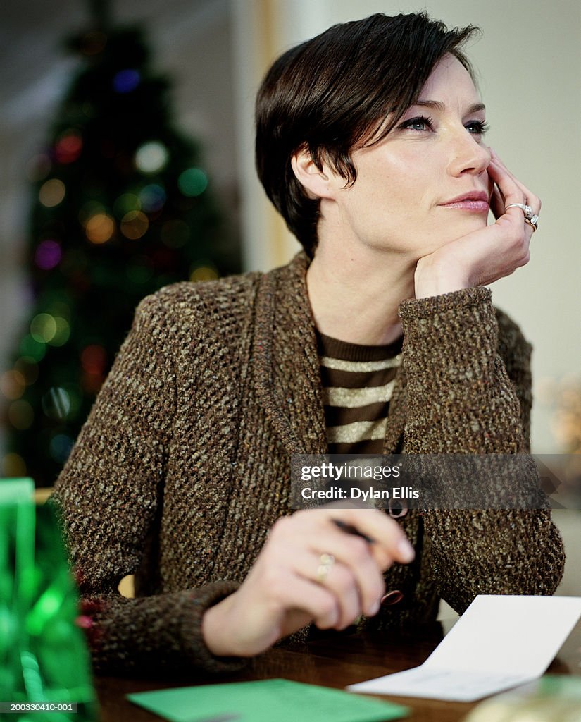 Woman sitting at table with  card, resting chin on hand