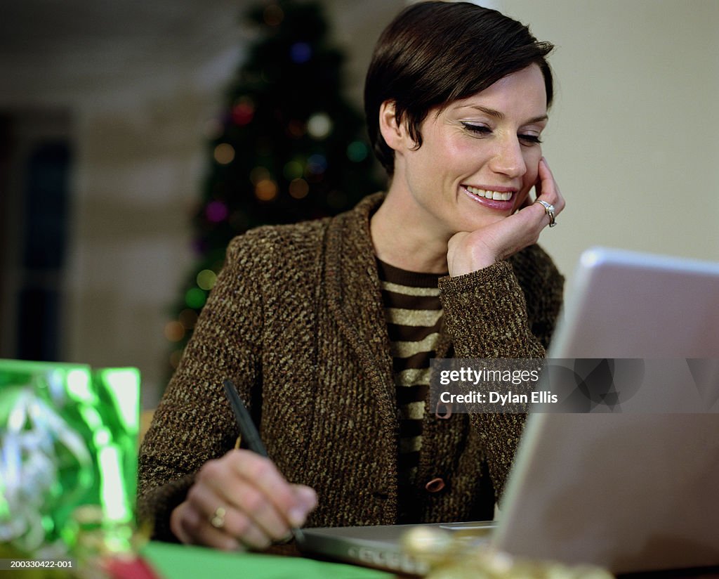 Woman sitting at laptop, resting chin on hand, smiling, focus on woman