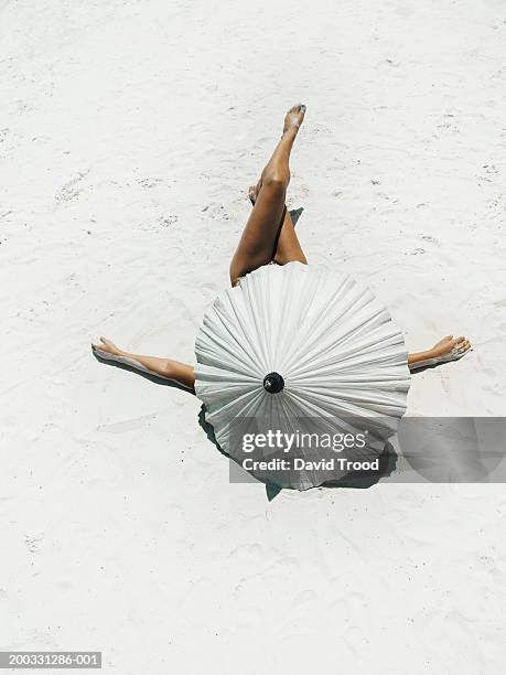 young woman lying on back protected by parasol on beach, rear view - tanned body stock pictures, royalty-free photos & images