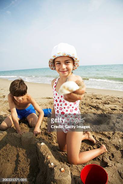 boy and girl (8-10) playing on beach, girl holding out shell, portrait - short hair photos et images de collection