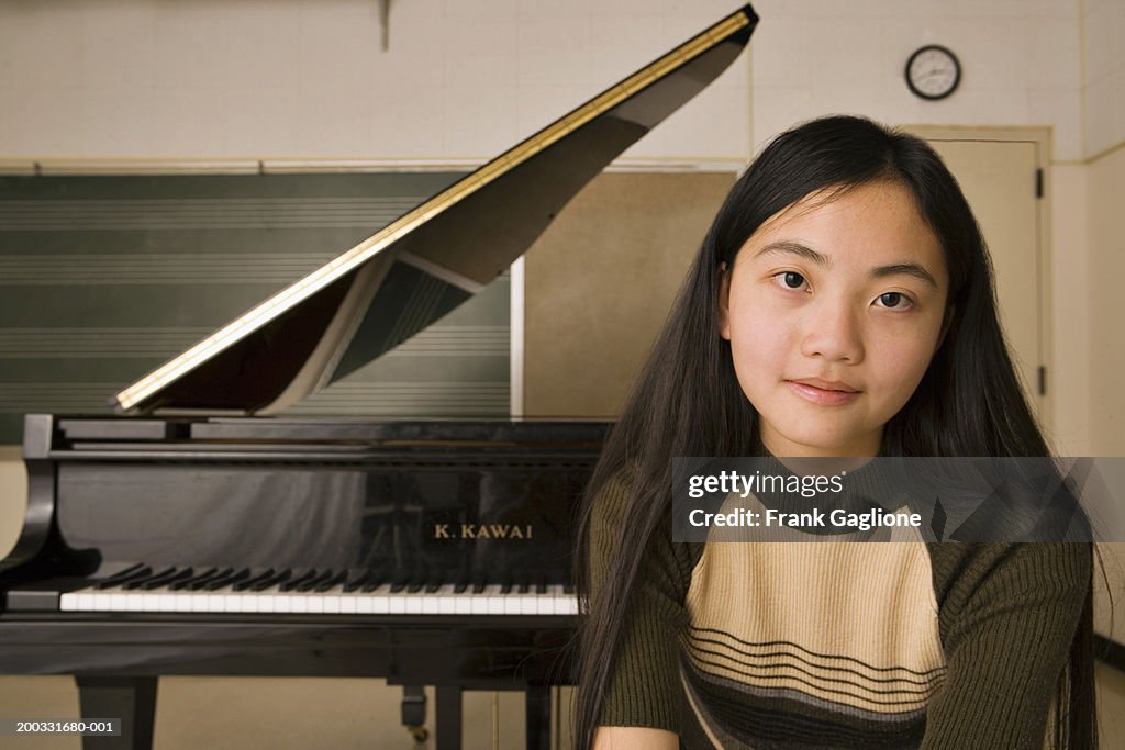 Teenage girl (12-14) sitting in front of piano in classroom, portrait