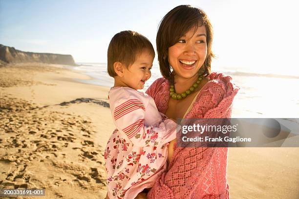 mother holding toddler girl (21-24 months), standing on beach, smiling - condado de san mateo imagens e fotografias de stock