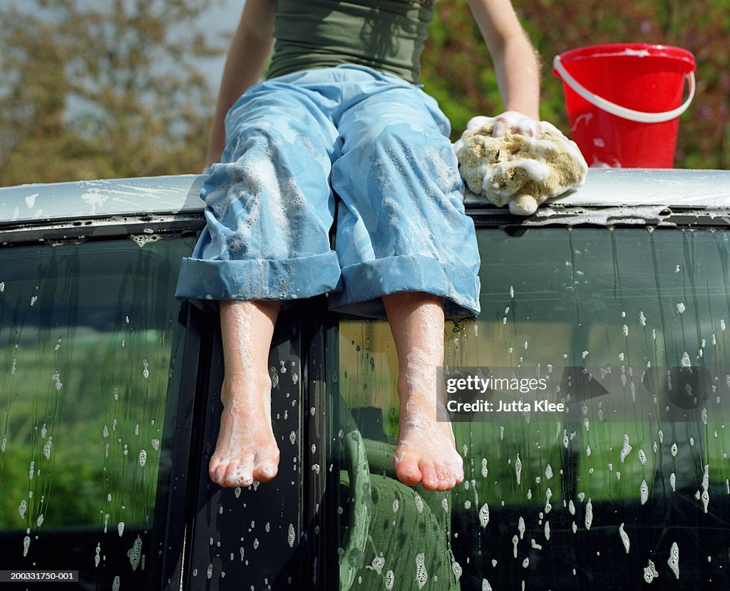 Girl (7-9) sitting on car roof while washing car, low section