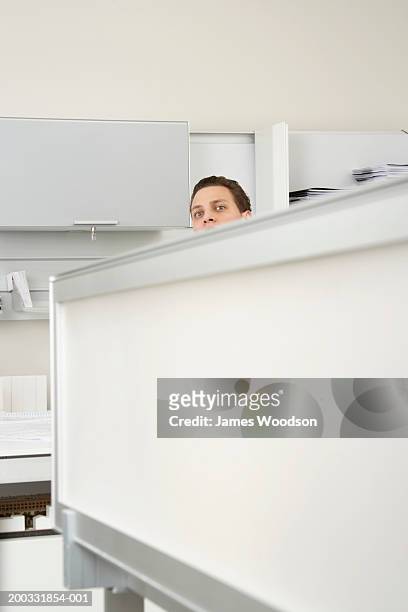 young businessman peering over desk divider in office, high section - ergens overheen kijken stockfoto's en -beelden
