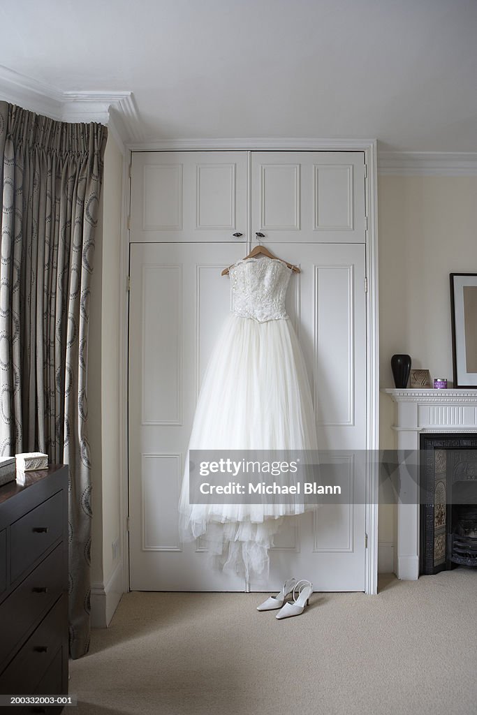 Wedding dress hanging on wardrobe doors, white shoes on floor