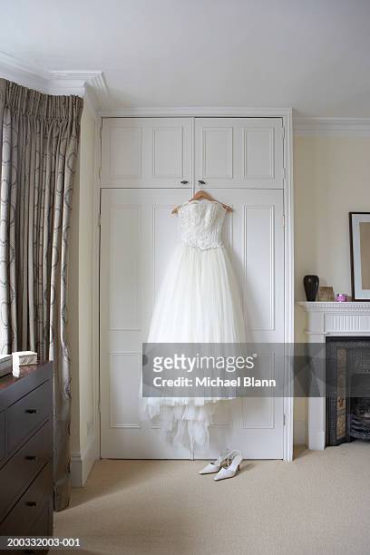 wedding dress hanging on wardrobe doors, white shoes on floor - robe de mariée photos et images de collection