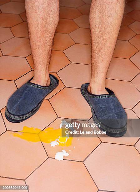 man in slippers standing over broken egg, low section - hairy man stockfoto's en -beelden