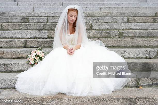 bride sitting on stone steps, looking towards ground - sposa foto e immagini stock