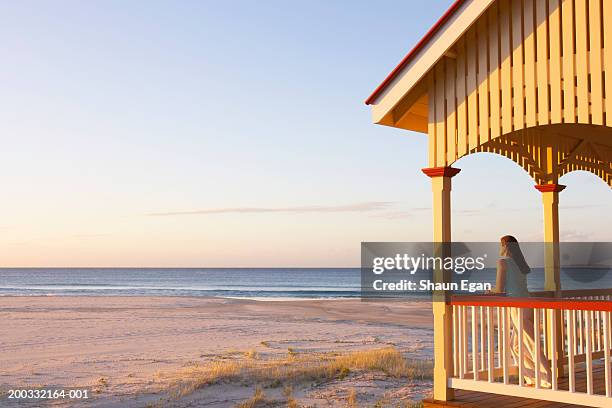 woman leaning on balcony by beach, sunset - beach house stock pictures, royalty-free photos & images