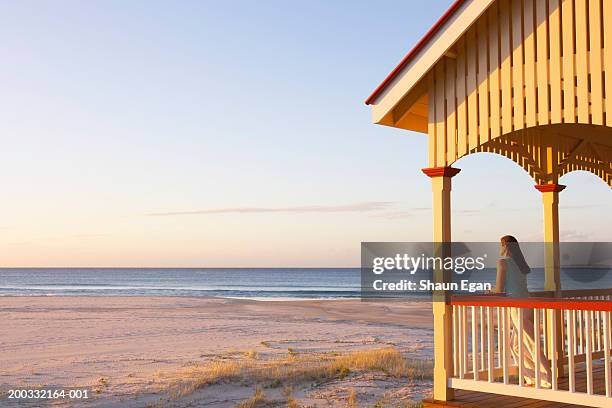 woman leaning on balcony by beach, sunset - beach house balcony stock pictures, royalty-free photos & images