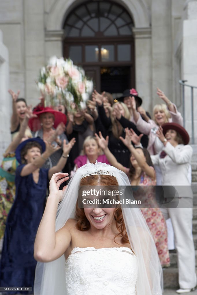 Bride throwing bouquet over head to crowd standing on steps to church