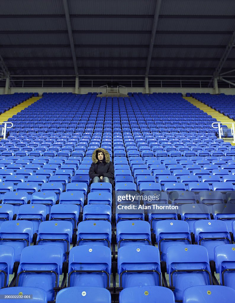 Man sitting amongst rows of blue seats in stadium