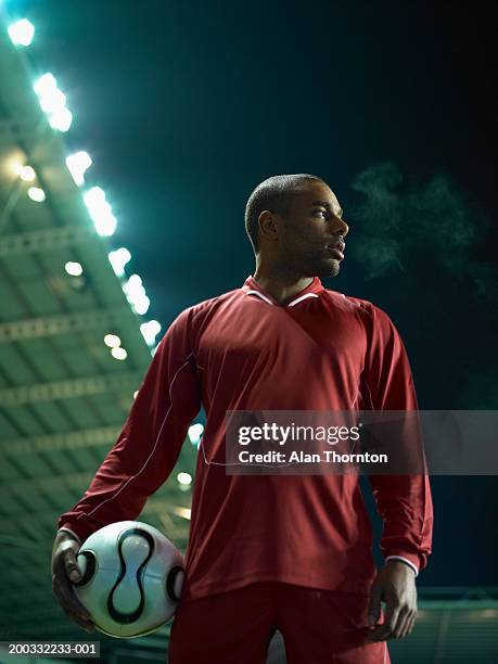 young male football player holding ball, night, low angle view - alan ball fútbol fotografías e imágenes de stock