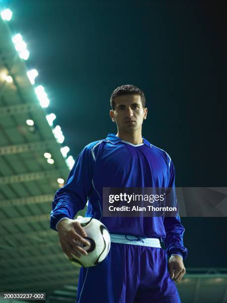 young male football player holding ball, portrait, night - alan ball fútbol fotografías e imágenes de stock