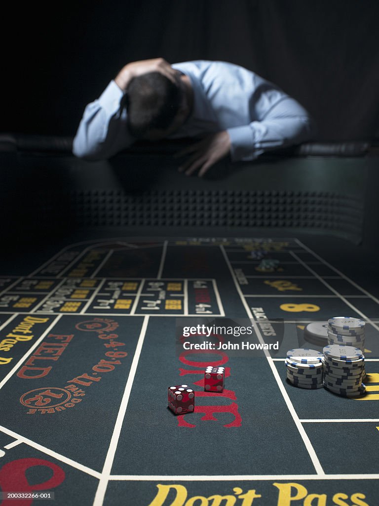 Man slumped at craps table, holding head (focus on table)