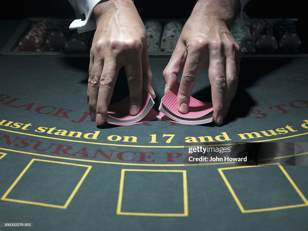 Male croupier shuffling cards at table, merging two piles, close-up