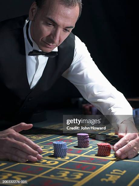 male croupier reaching for stacked bets at roulette table - casino dealer fotografías e imágenes de stock