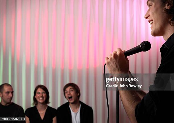 young male stand-up comedian performing on stage, audience laughing - comedian audience stock pictures, royalty-free photos & images