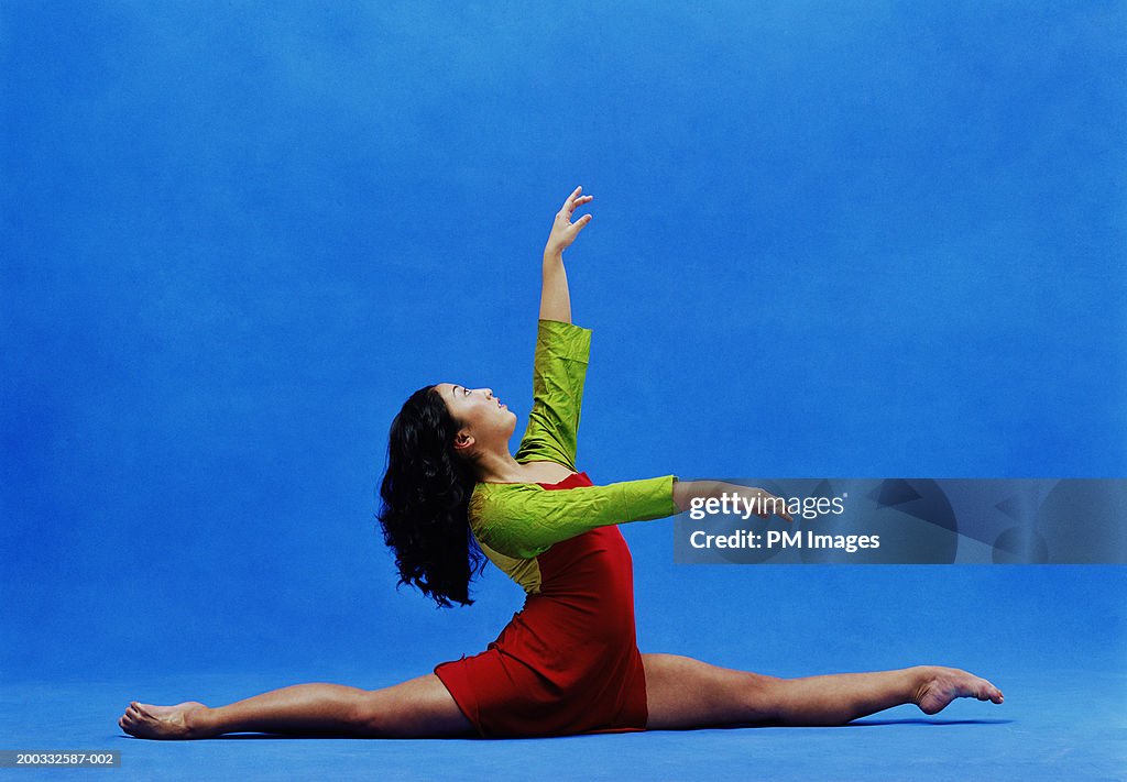 Young female dancer doing the splits on floor, arms raised, side view