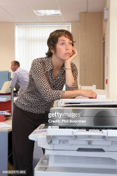 woman leaning on photocopier in office, chin in hand - drudgery stock pictures, royalty-free photos & images