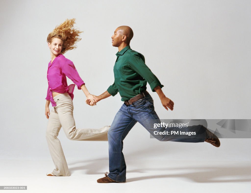 Young man and woman running, holding hands, side view