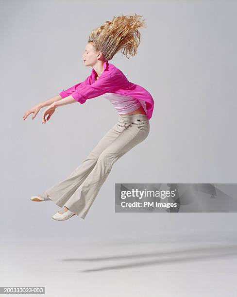 young woman flying backwards, arms extended, side view - grey trousers stock-fotos und bilder