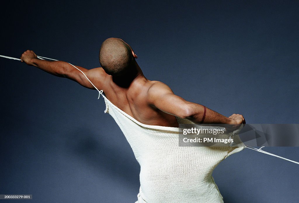 Man breaking free from fabric, rear view
