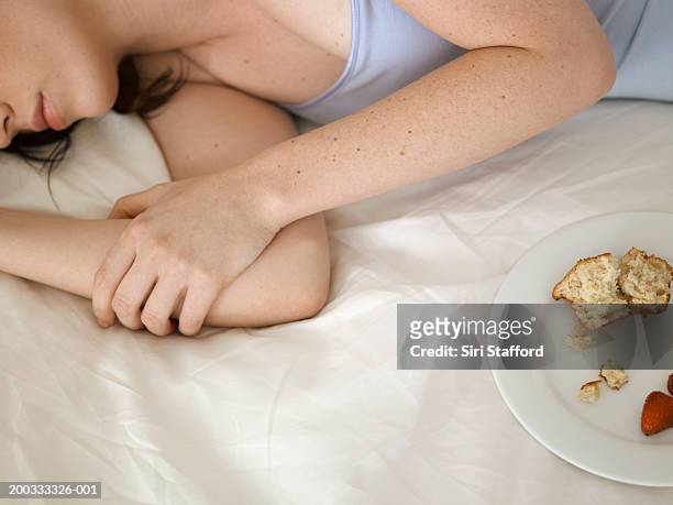young woman lying on bed, leftover food on plate - cami stockfoto's en -beelden