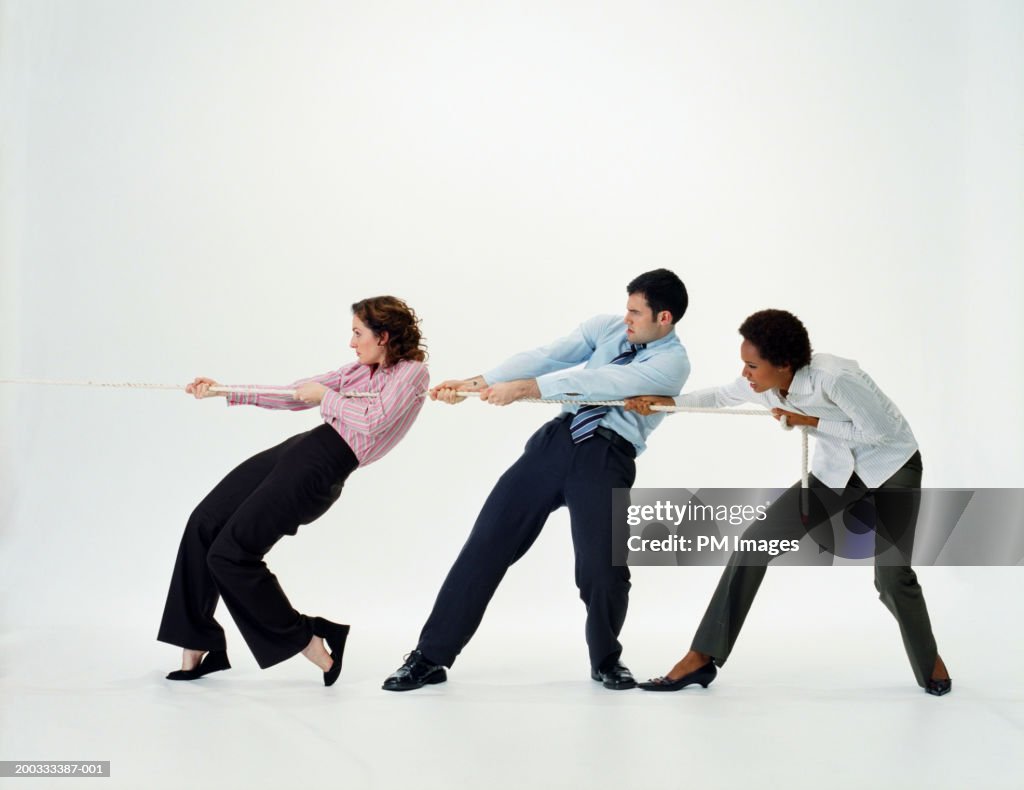 Two businesswomen and businessman pulling rope, side view