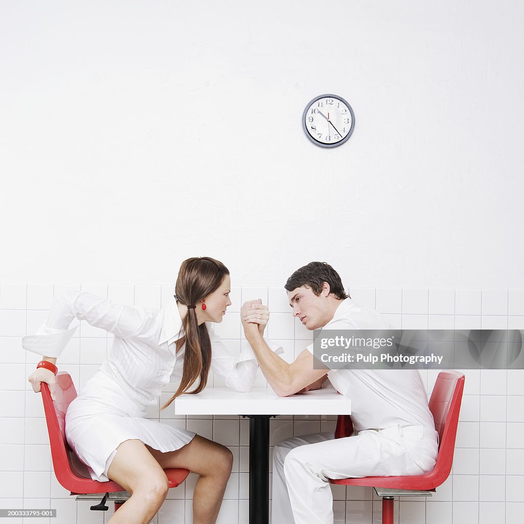 Young couple sitting at table, arm wrestling, side view