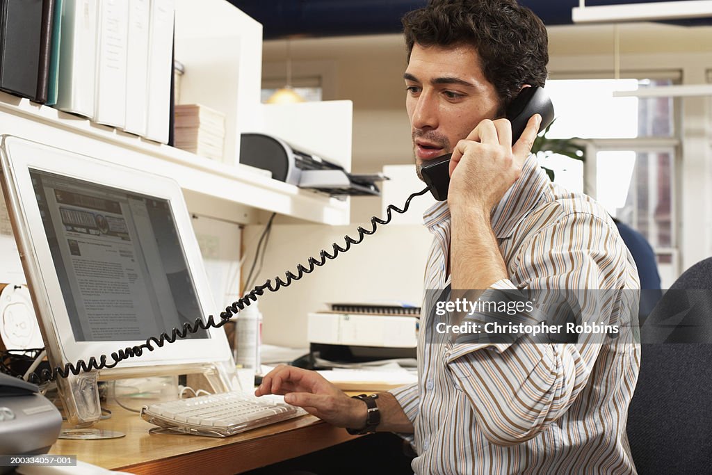 Male office worker with sleeves rolled up, using telephone