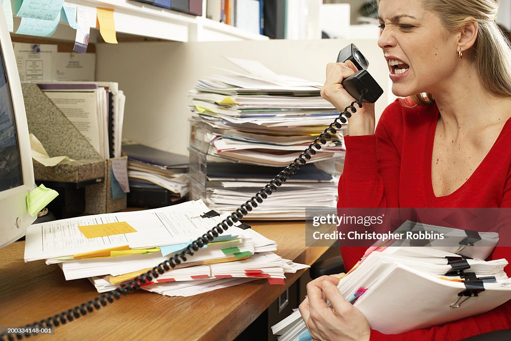 Female office worker holding paperwork, snarling at phone handset