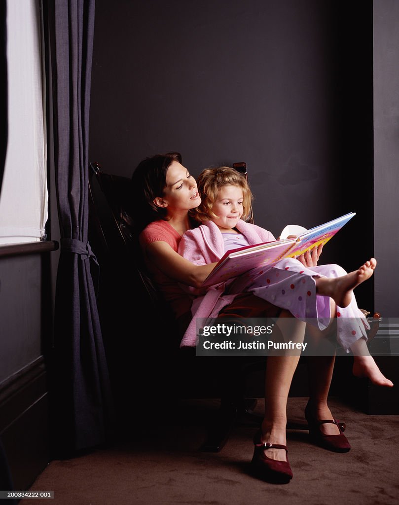 Girl (6-8) sitting on mother's lap, reading book