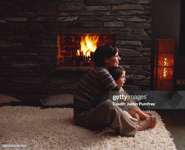 mother and daughter (4-6) embracing by fireplace, side view - sitting by fireplace stock pictures, royalty-free photos & images