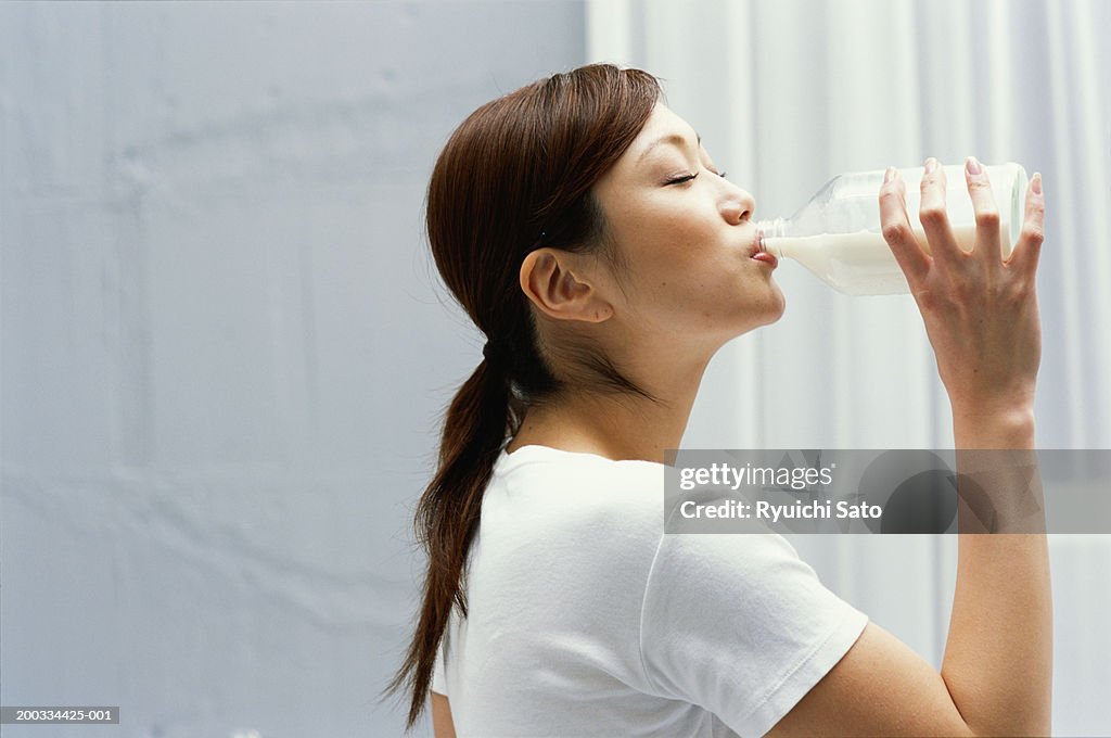 Young woman drinking from milk bottle, eyes closed, side view