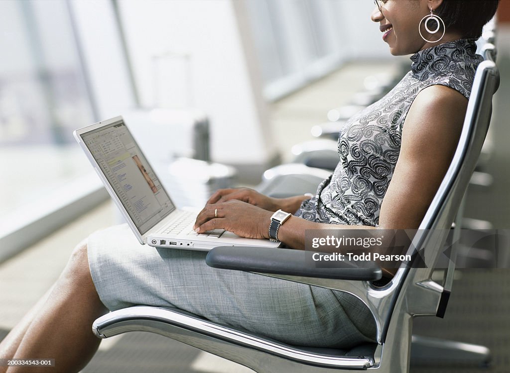 Woman using laptop in airport lounge, side view, mid section