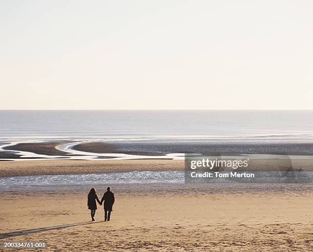 couple walking on beach, holding hands, rear view - camber sands ストックフォトと画像