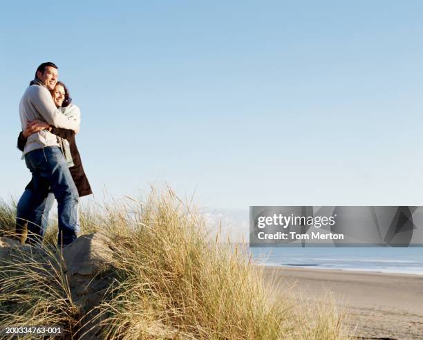 couple embracing, standing in long grass on sand dune, low angle view - couple dunes stock-fotos und bilder