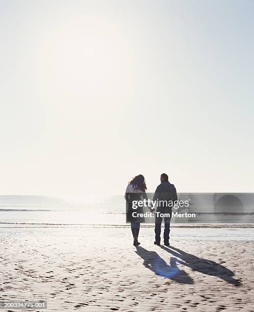 couple holding hands, walking on beach, rear view (sun flare) - sun flare couple stock-fotos und bilder