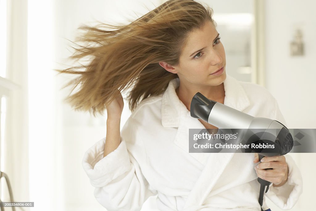 Young woman blowdrying hair, wearing dressing gown